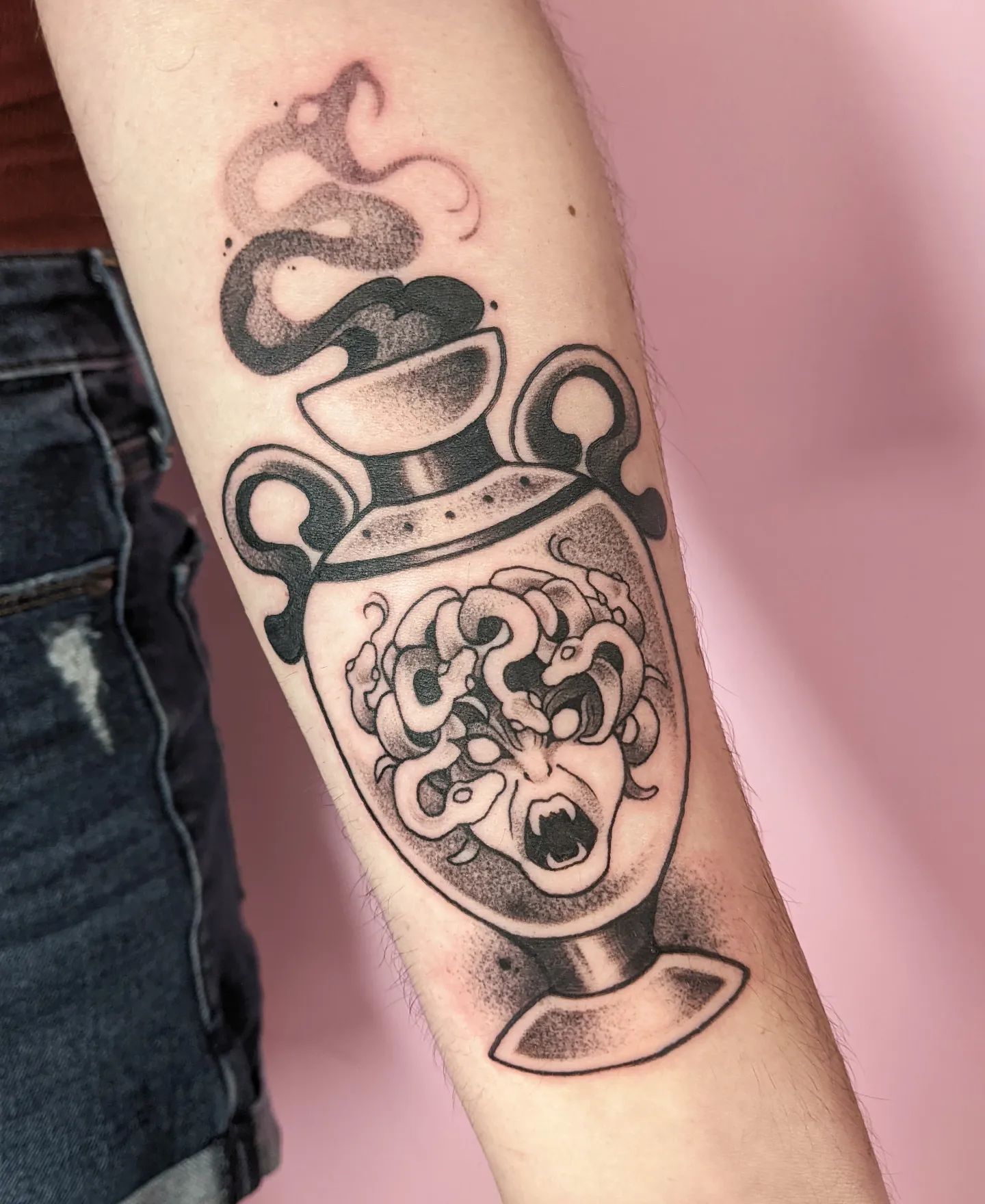 A black and gray tattoo of an amphora has a gorgon's head in the middle of it and you are sure to look amazing.