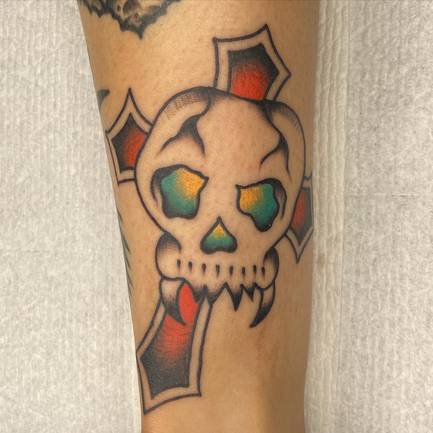 Skull tattoo lovers will adore this tattoo a lot. A scary skull is placed in the middle of a cross. The colors used take this tattoo a whole different level. In the cross, black and red shades offer a strong look while yellow and blue shades used in the skull are fun.