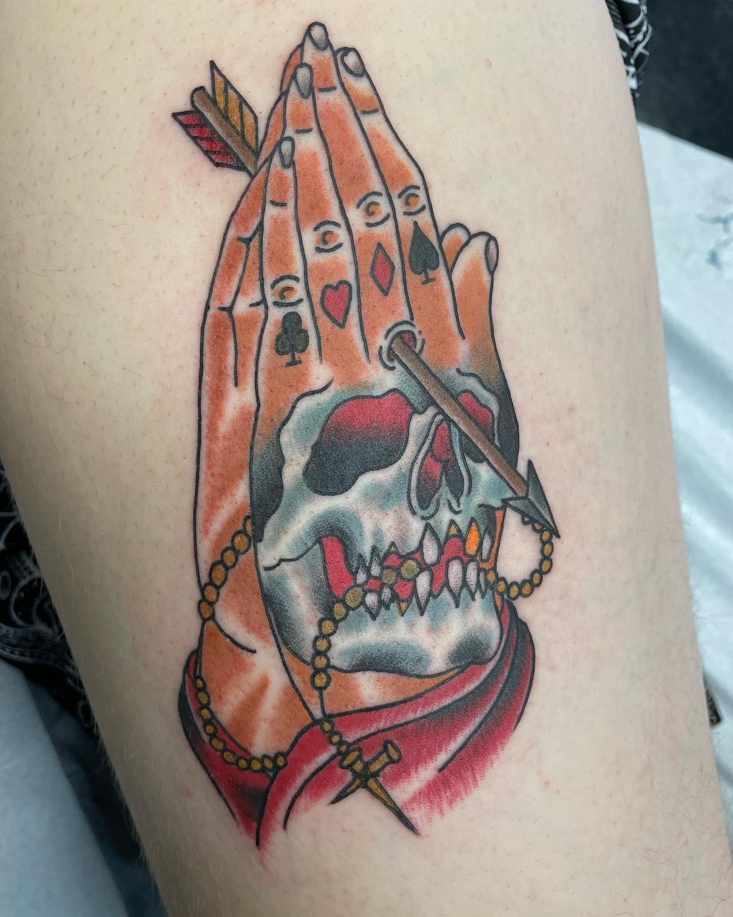 If you want to get a quirky and fun prayer hands tattoo, this one may be a perfect choice. A skeleton and arrow look amazing with colorful details.