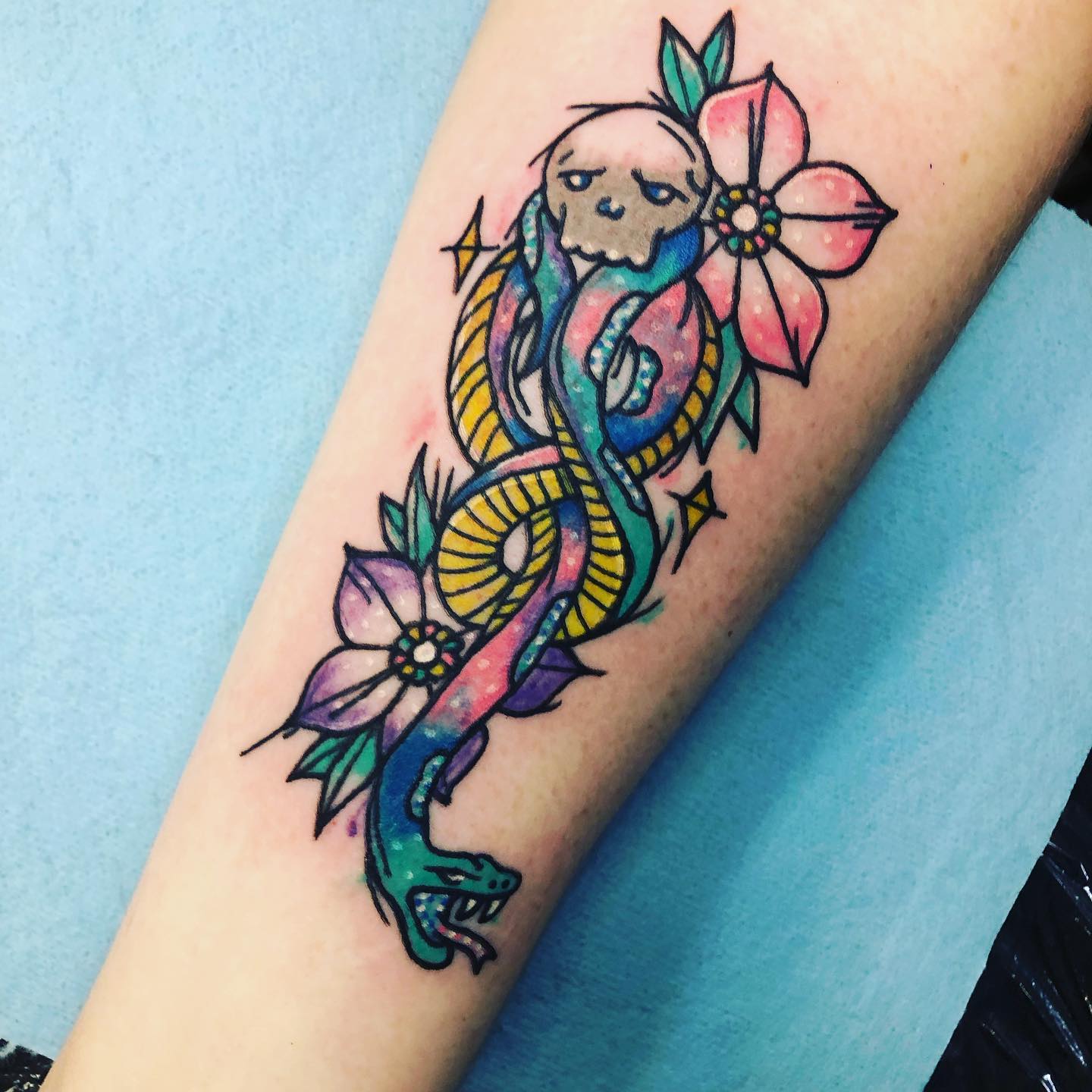 What a cool and colorful tattoo! The floral theme is really beautiful and well-executed, and it is nice to see how the Death Eater logo can be transformed into something unique and sweet like this.