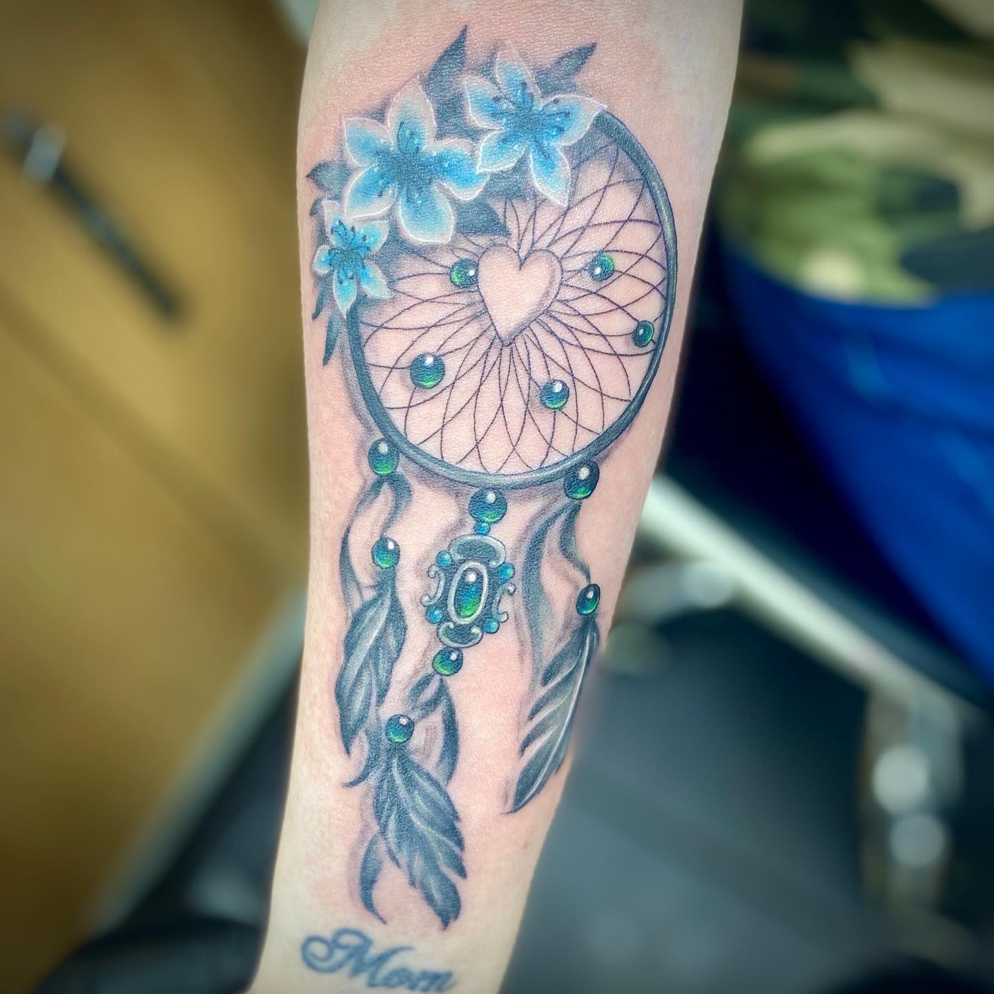 If you want to take your dream catcher tattoo to a whole different level, go for the tattoo above. Blue dreamcatcher tattoo with green stones is a tattoo for those who want to show their love of nature and their connection with the earth. The color blue represents the sky, and green is associated with trees, plants, and life. Plus, you show your love with the heart shape in the center.