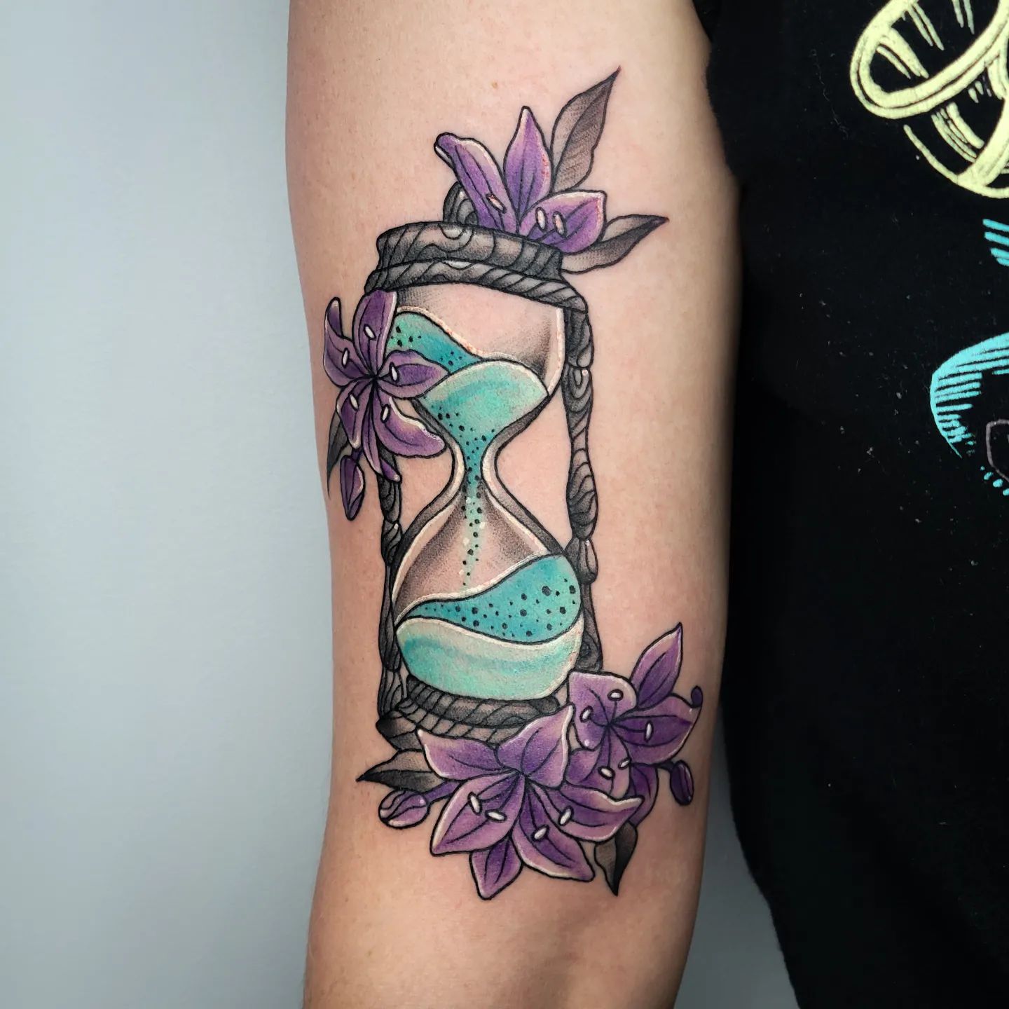 Sandglass and purple lilies tattoo is a symbol of the meaning of life, nature, and eternity. It is said that the sandglass represents the passage of time and how we should not waste it but rather make the most out of it. The lilies are a symbol of purity and light, so they are meant to represent the hope that we will be able to attain purity in our lives.