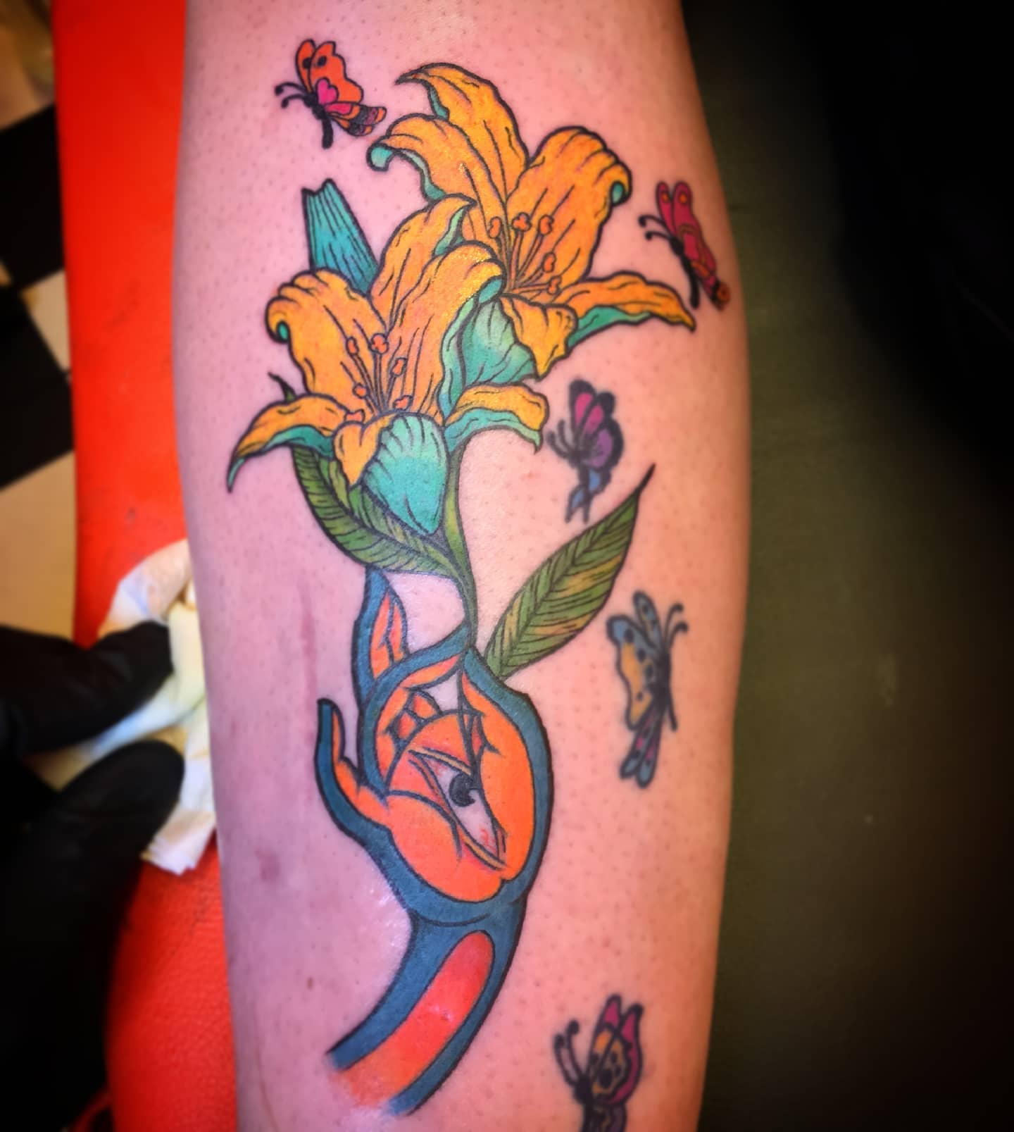 Old school colorful lily tattoo is a tattoo that has been around for a long time. The colors are bright and vibrant, and the design is relatively simple. In the example above, a hand with an eye is holding the lillies and butterflies are flying. If you like creative tattoos, give it a shot.