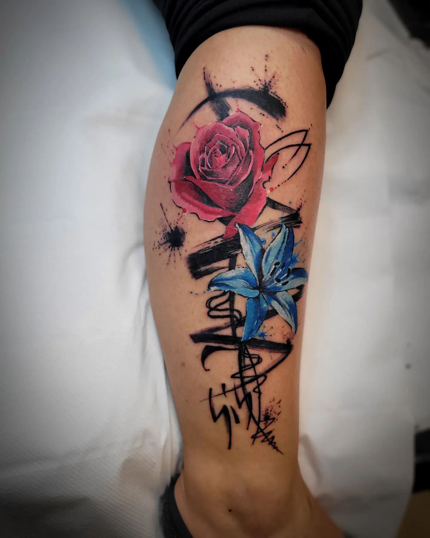 Red rose and blue lily tattoo is a symbol of love. It means that the one you love loves you back. It can also mean that your love for someone is unconditional and true. Black splash behind makes them stand out, too.