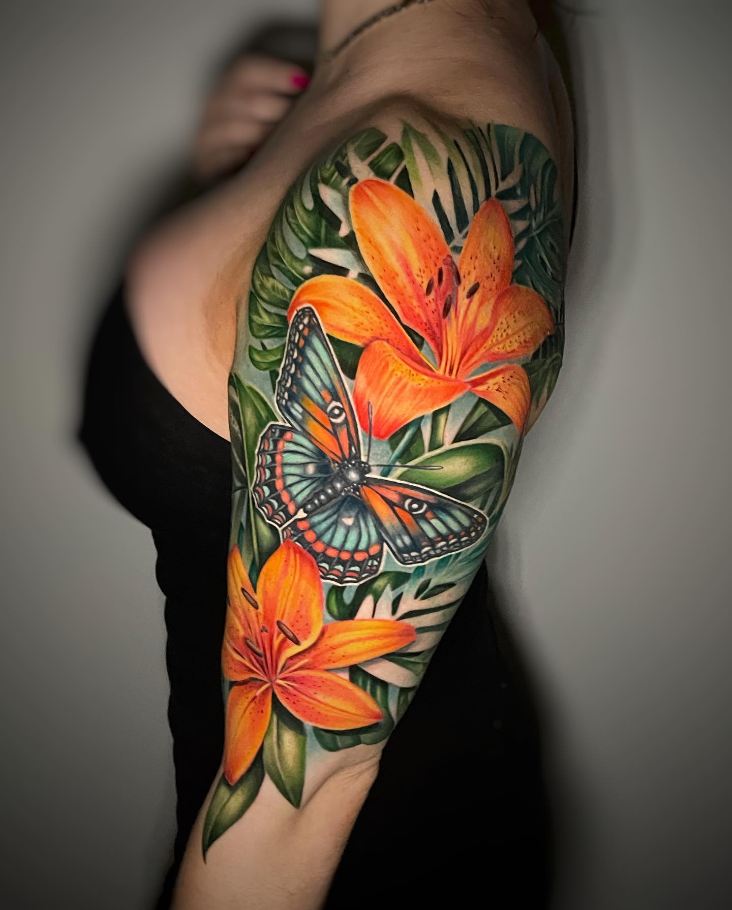 Want to cover up your upper arm with lilies? If your answer is yes, the colorful and vivid tattoo design is for you! The color palette includes green, orange and blue. Besides realistic orange lilies, a butterfly is used to make this tattoo greater.