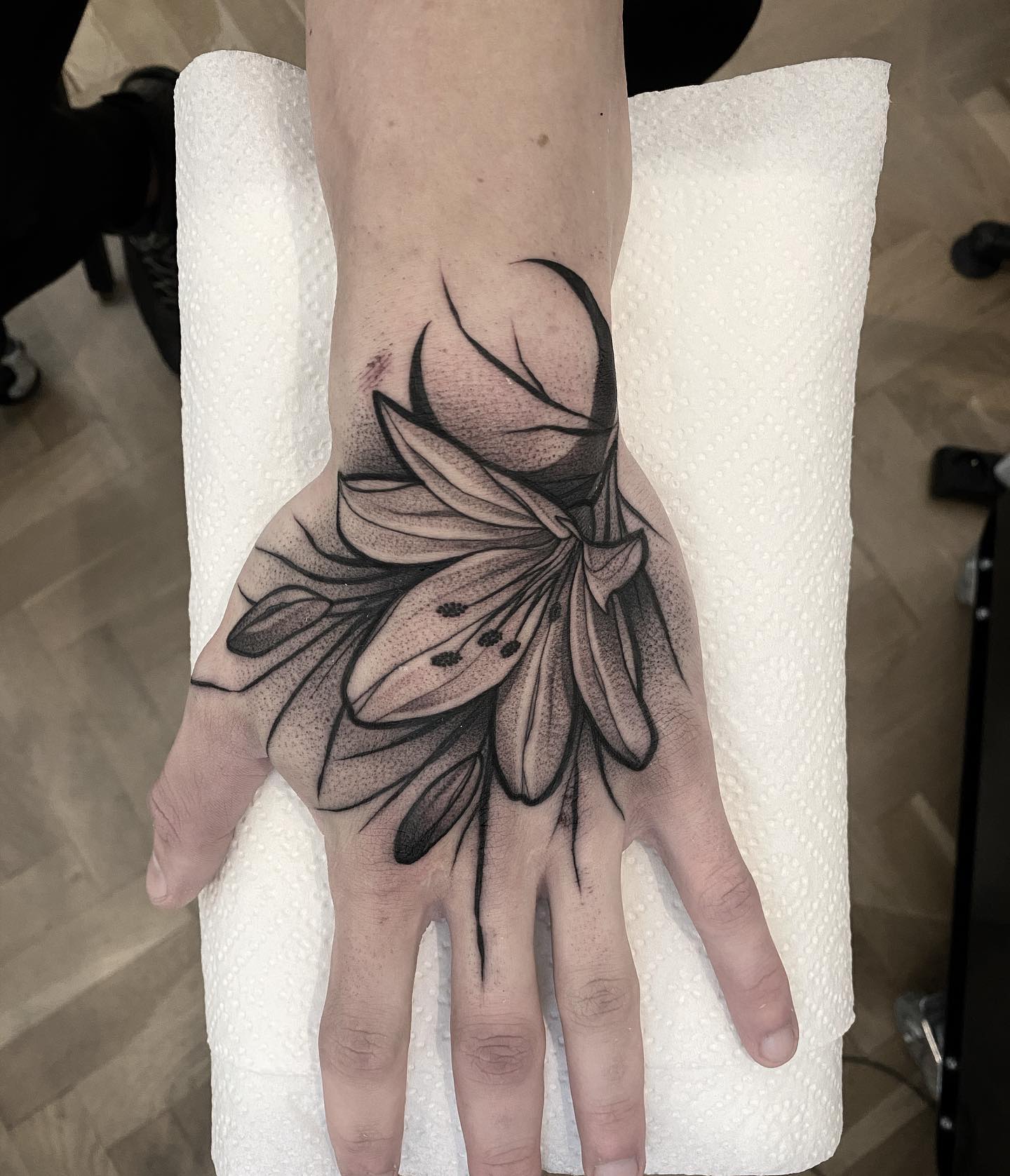 Dotwork lily tattoo on hand is a very unique design. It has small dots that are connected together to form the petals of a flower. If you are brave to cover your hand with a lily, go for it.