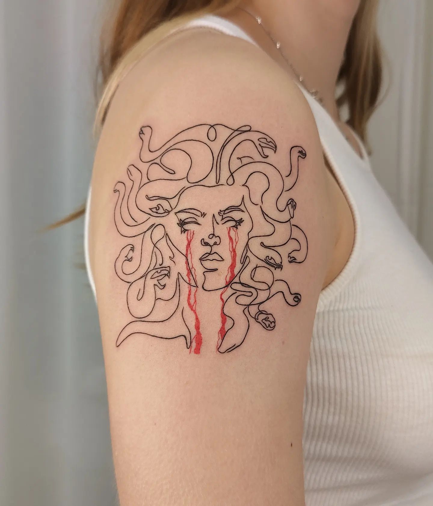 Line work tattoos may seem simple but actually they offer a gorgeous look for those who want a minimalist tattoo. In this design, black ink is used to create the shape of medusa and for her tears, red ink is used to make them stand out more.